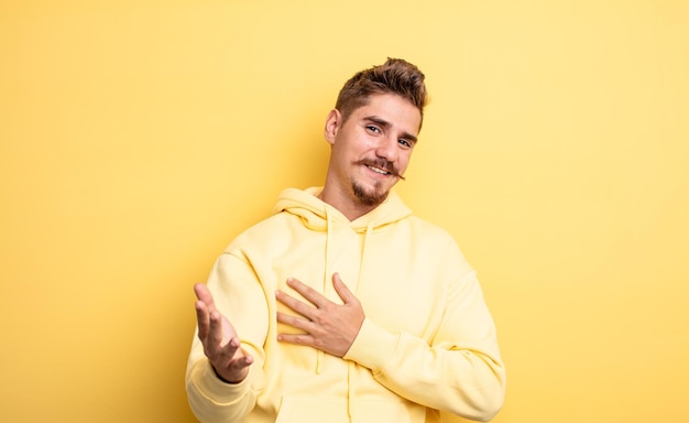 Young handsome man feeling happy and in love, smiling with one hand next to heart and the other stretched up front. strange moustache concept