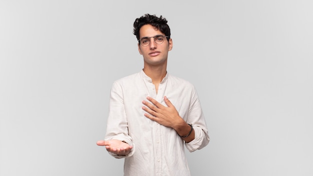 Young handsome man feeling happy and in love, smiling with one hand next to heart and the other stretched up front