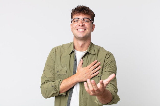 Young handsome man feeling happy and in love, smiling with one hand next to heart and the other stretched up front