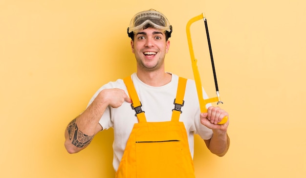 Young handsome man feeling happy and pointing to self with an excited handyman concept
