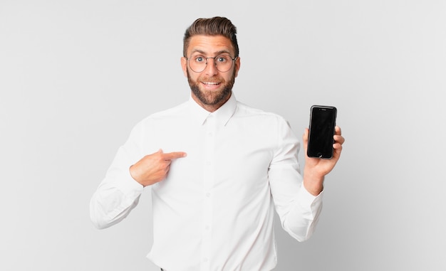 young handsome man feeling happy and pointing to self with an excited and holding a cell