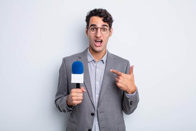 Young handsome man feeling happy and pointing to self with an\
excited. presenter with microphone