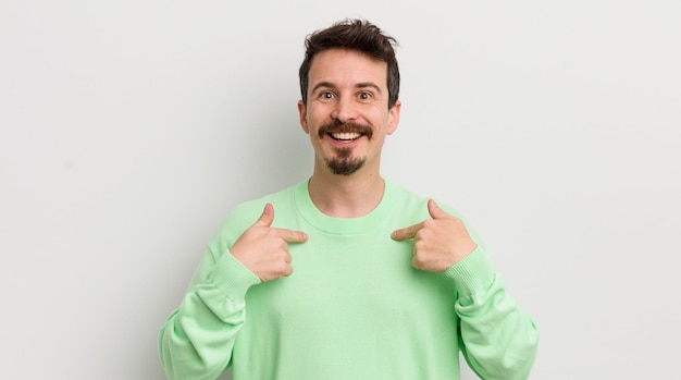 Young handsome man feeling happy and pointing to self with an excited