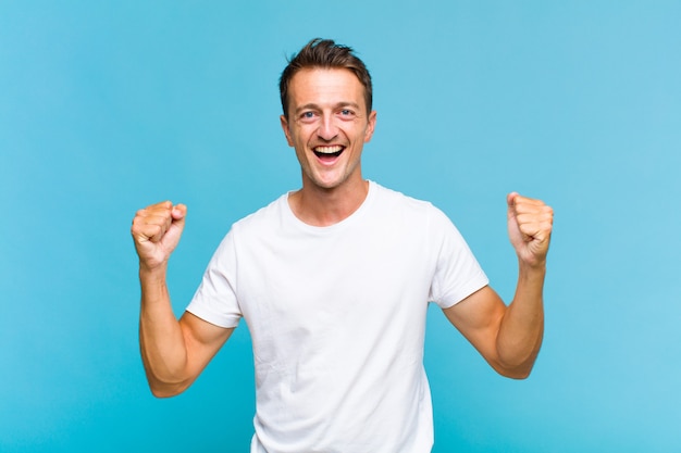 Young handsome man feeling happy, positive and successful, celebrating victory, achievements or good luck