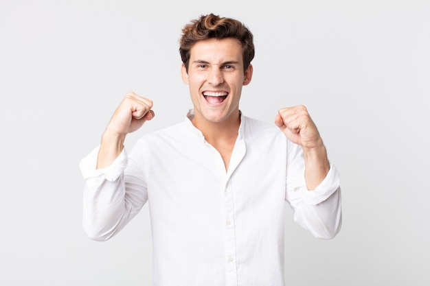 Young handsome man feeling happy, positive and successful, celebrating victory, achievements or good luck