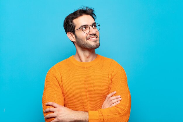 Giovane uomo bello che si sente felice, orgoglioso e speranzoso, chiedendosi o pensando, alzando lo sguardo per copiare lo spazio con le braccia incrociate