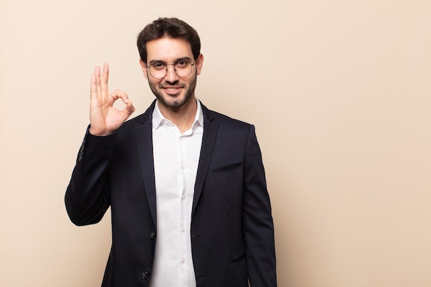 Giovane uomo bello sentirsi felice, rilassato e soddisfatto, mostrando approvazione con un gesto ok, sorridendo