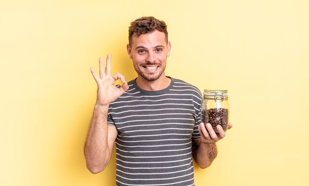 Young handsome man feeling happy, showing approval with okay gesture coffee beans concept