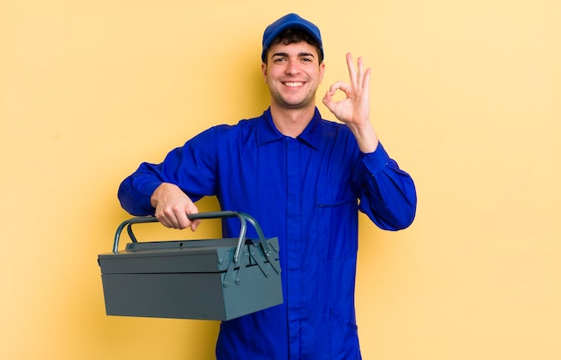 Young handsome man feeling happy showing approval with okay gesture plumber concept