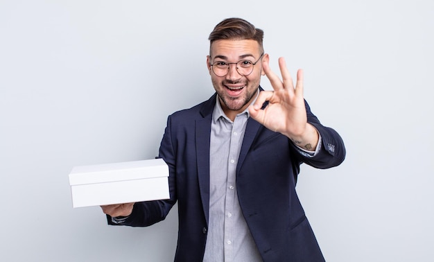 Young handsome man feeling happy, showing approval with okay gesture. white box concept
