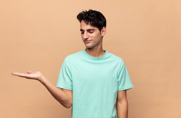 Young handsome man feeling happy and smiling casually, looking to an object or concept held on the hand on the side