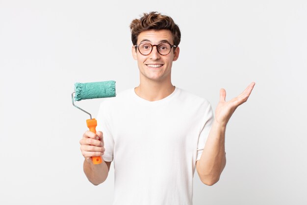 Young handsome man feeling happy, surprised realizing a solution or idea and holding a roller paint