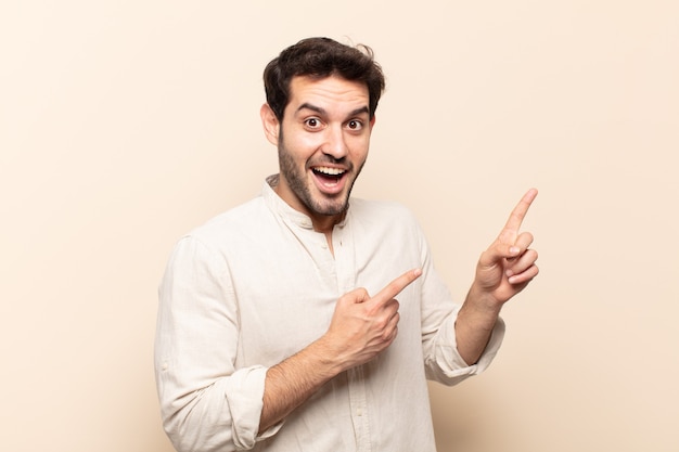 Young handsome man feeling joyful and surprised, smiling with a shocked expression and pointing to the side