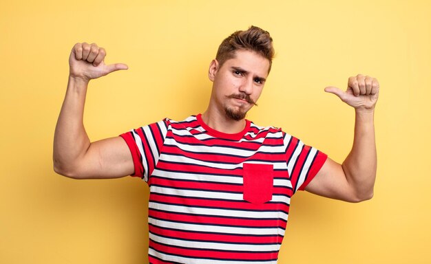 Young handsome man feeling proud, arrogant and confident, looking satisfied and successful, pointing to self. strange moustache concept