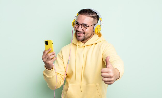 Young handsome man feeling proud,smiling positively with thumbs up. headphones and smartphone concept