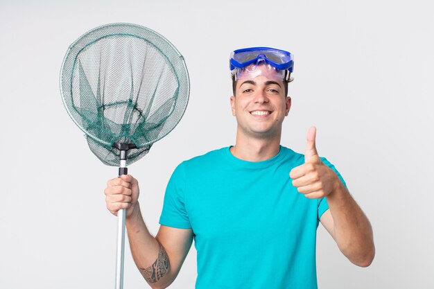 Young handsome man feeling proud,smiling positively with thumbs up with goggles and fishing net