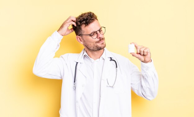 Young handsome man feeling puzzled and confused, scratching head. physician pills bottle concept