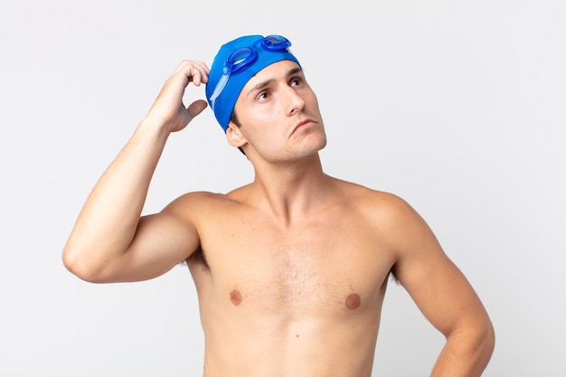 Young handsome man feeling puzzled and confused, scratching head. swimmer concept