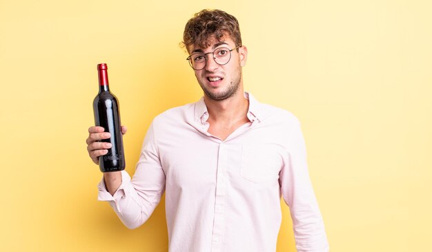 Young handsome man feeling puzzled and confused. wine bottle concept