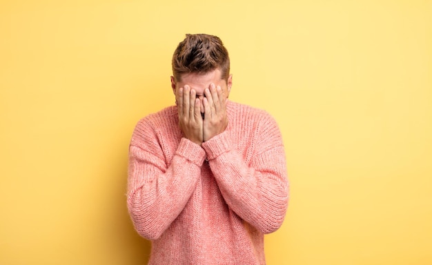 Young handsome man feeling sad, frustrated, nervous and depressed, covering face with both hands, crying. strange moustache concept