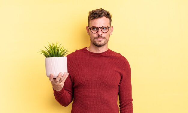 young handsome man feeling sad, upset or angry and looking to the side. decorative plant concept