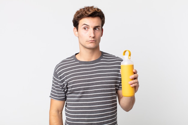 Young handsome man feeling sad, upset or angry and looking to the side and holding a coffee thermos