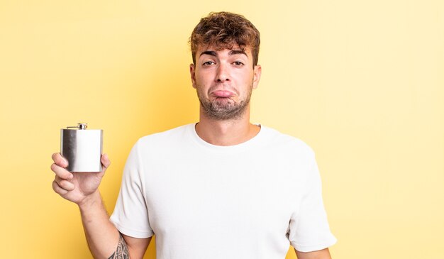 Young handsome man feeling sad and whiney with an unhappy look and crying. alcohol flask concept