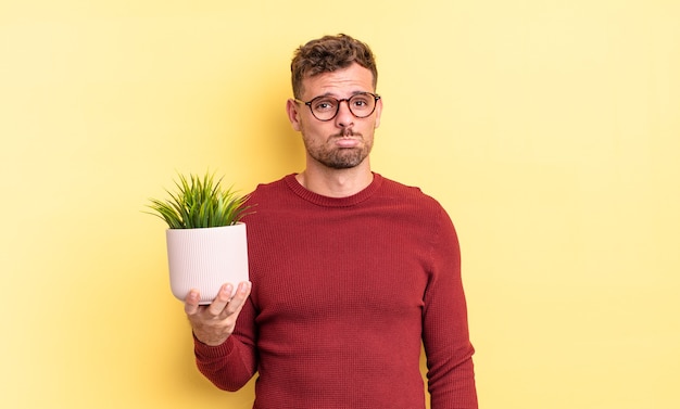 Young handsome man feeling sad and whiney with an unhappy look and crying. decorative plant concept