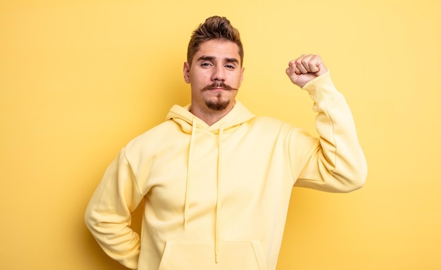 Young handsome man feeling serious, strong and rebellious, raising fist up, protesting or fighting for revolution. strange moustache concept