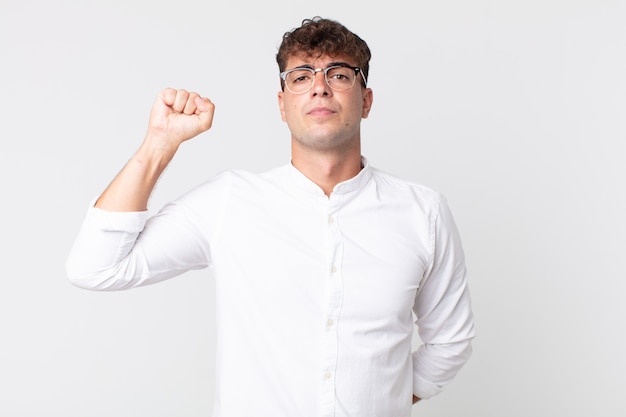 Young handsome man feeling serious, strong and rebellious, raising fist up, protesting or fighting for revolution