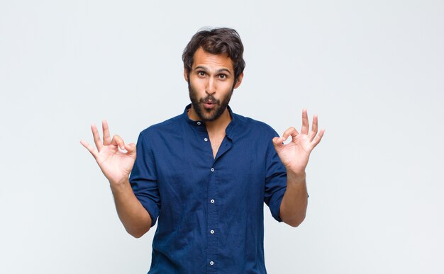 Young handsome man feeling shocked, amazed and surprised, showing approval making okay sign with both hands