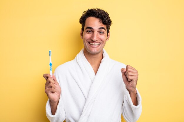 Young handsome man feeling shocked,laughing and celebrating success. bathrobe and toothbrush concept