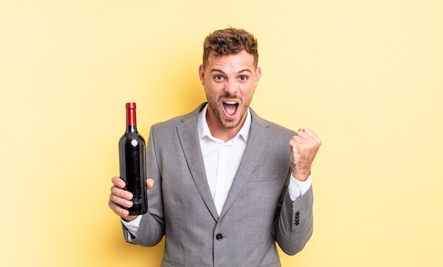 Young handsome man feeling shocked,laughing and celebrating success. bottle of wine concept