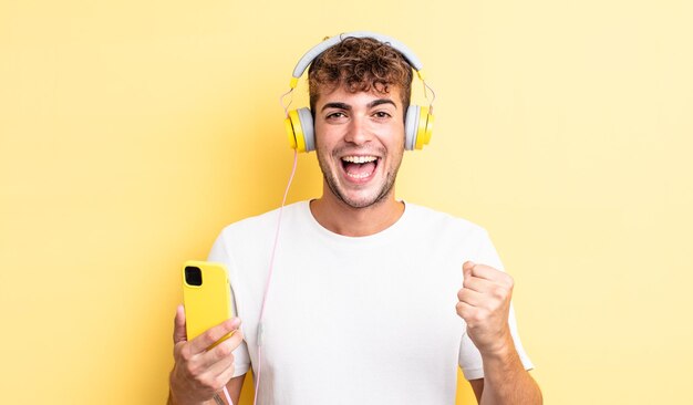 Young handsome man feeling shocked,laughing and celebrating success. headphones and smartphone concept