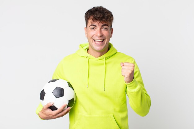 젊고 잘생긴 남자는 충격을 받고 웃고 성공을 축하하고 축구공을 들고 있다