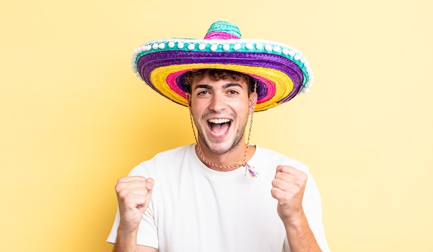 젊은 잘생긴 남자는 충격을 받고 웃고 성공을 축하합니다. 멕시코 모자 개념