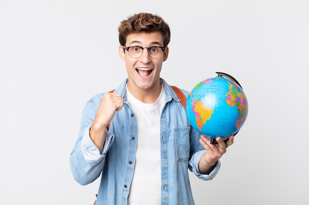 젊은 잘생긴 남자는 충격을 받고 웃고 성공을 축하합니다. 세계 지도를 들고 있는 학생