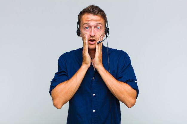 Young handsome man feeling shocked and scared, looking terrified with open mouth and hands on cheeks