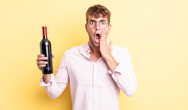 Young handsome man feeling shocked and scared. wine bottle concept