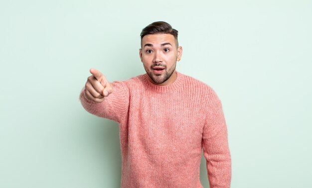 Young handsome man feeling shocked and surprised, pointing and looking upwards in awe with amazed, open-mouthed look