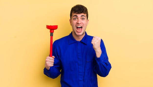 Young handsome man feeling shockedlaughing and celebrating success plumber concept