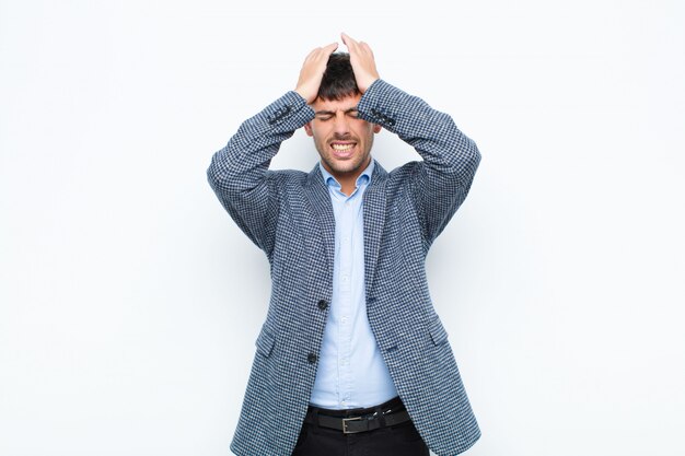 Foto giovane uomo bello sentirsi stressato e ansioso, depresso e frustrato con un mal di testa, alzando entrambe le mani a testa contro il muro bianco