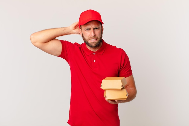 Giovane bell'uomo che si sente stressato, ansioso o spaventato, con le mani sulla testa hamburger che consegna il concetto