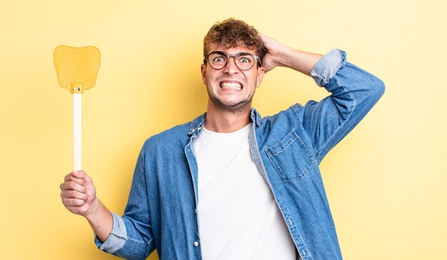 Young handsome man feeling stressed, anxious or scared, with hands on head. flyswatter concept