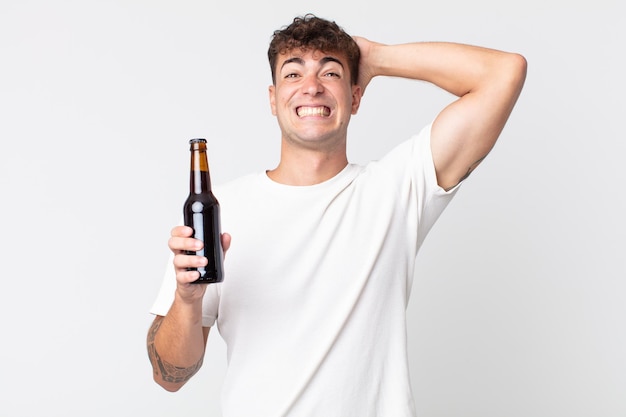 Young handsome man feeling stressed anxious or scared with hands on head and holding a beer bottle