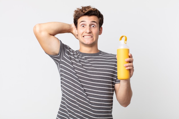 Young handsome man feeling stressed, anxious or scared, with hands on head and holding a coffee thermos