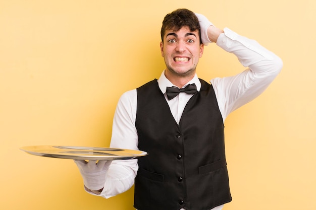 Young handsome man feeling stressed anxious or scared with hands on head waiter and tray concept