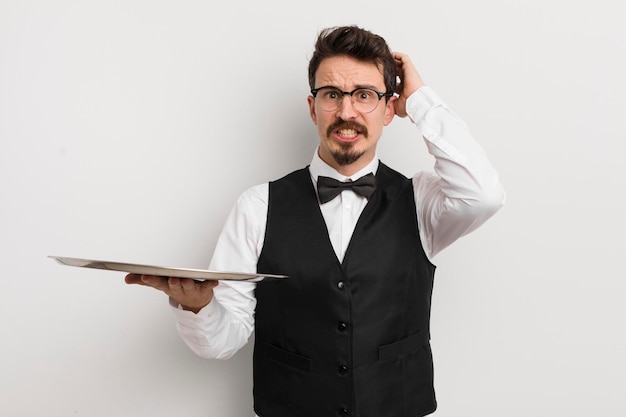 Young handsome man feeling stressed anxious or scared with hands on head waiter and tray concept