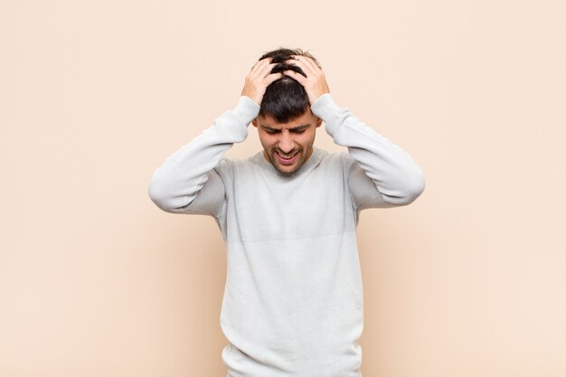 Young handsome man feeling stressed and frustrated, raising hands to head, feeling tired, unhappy and with migraine over warm wall