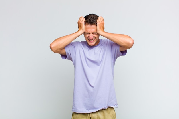 Young handsome man feeling stressed and frustrated, raising hands to head, feeling tired, unhappy and with migraine